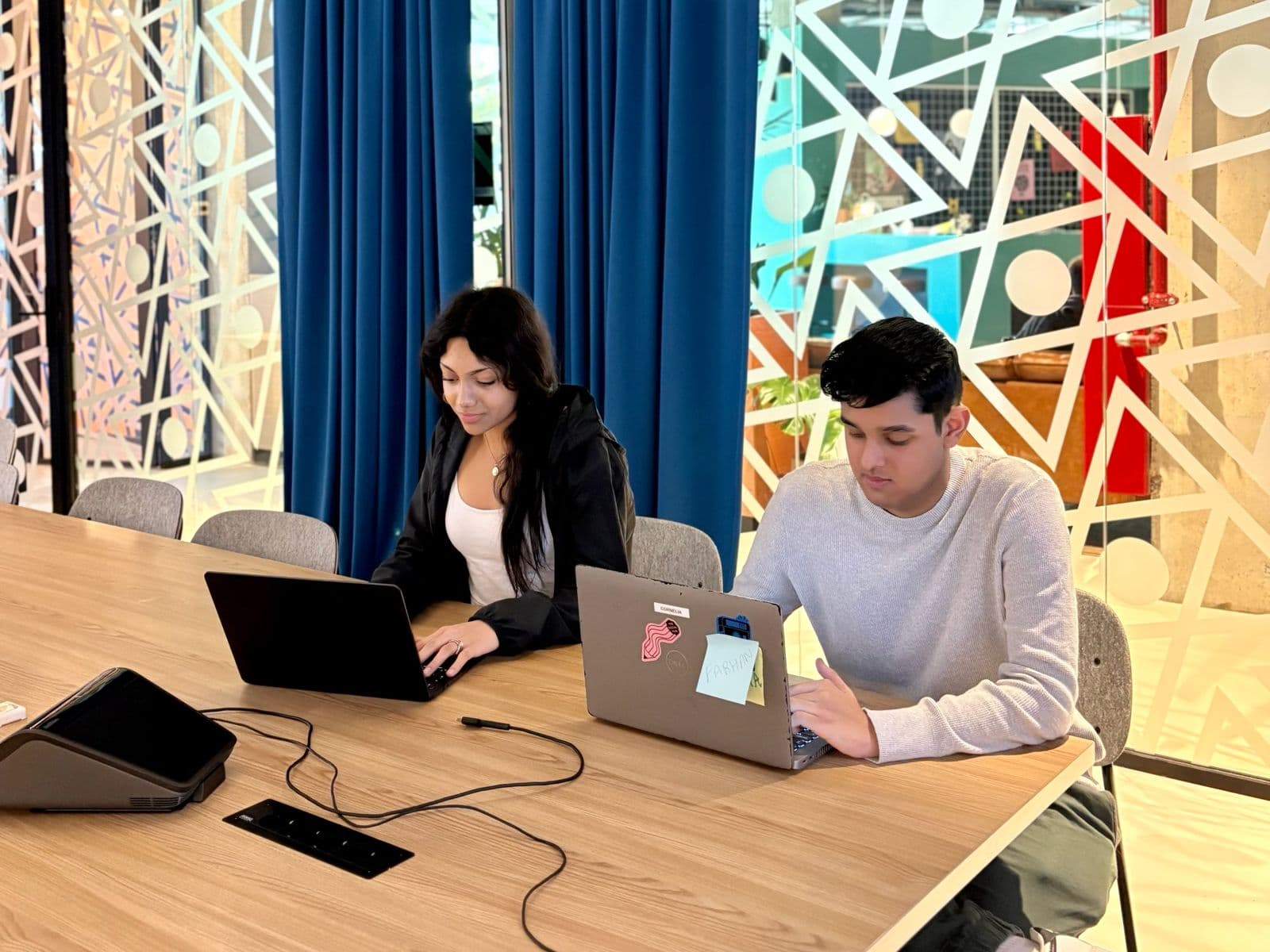 Two students working on laptops at a modern table — focused, flexible learning in a bright study space