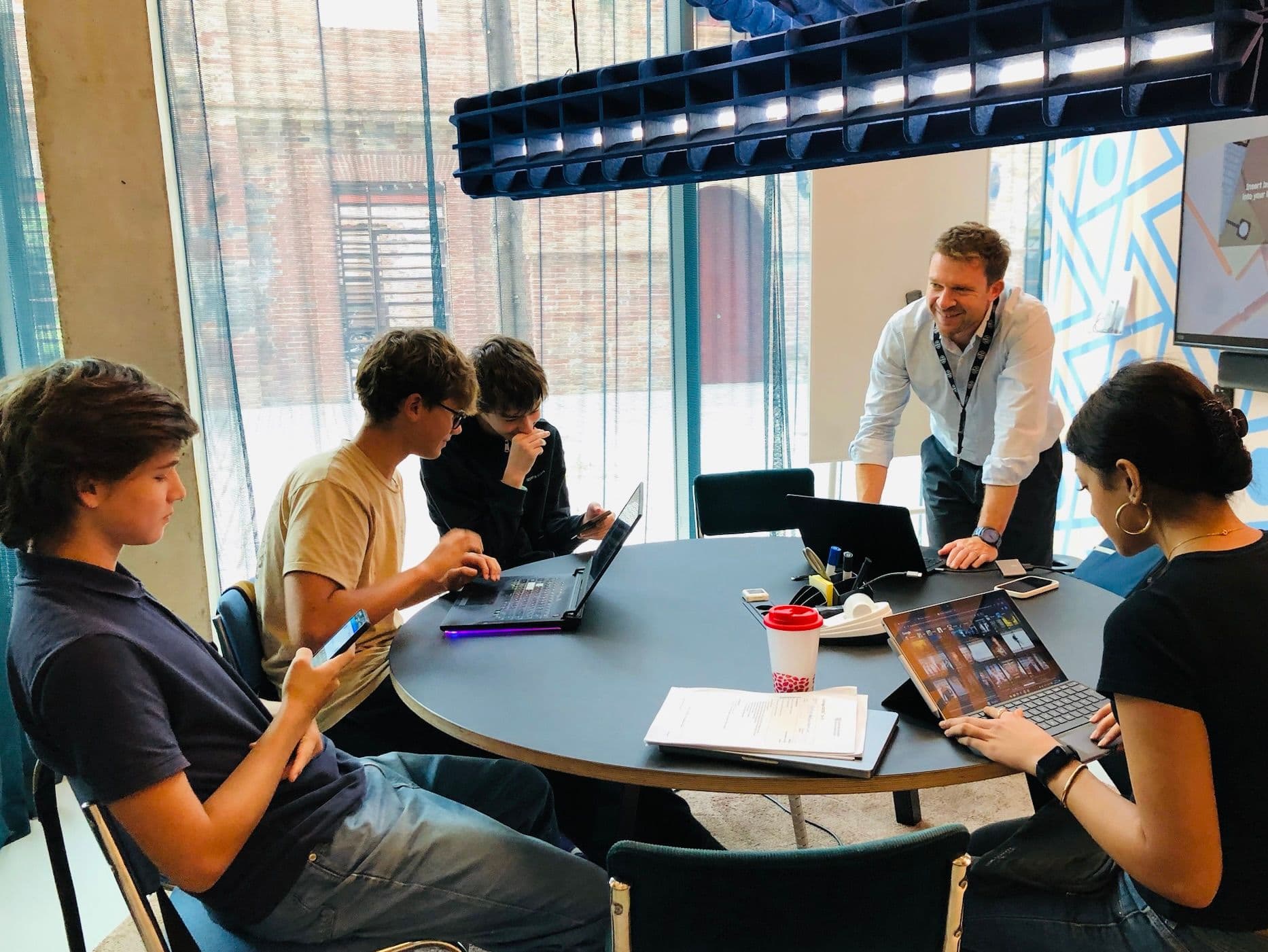 Small group collaborating in a bright, modern space — project-led learning and mentoring, not a classroom setup